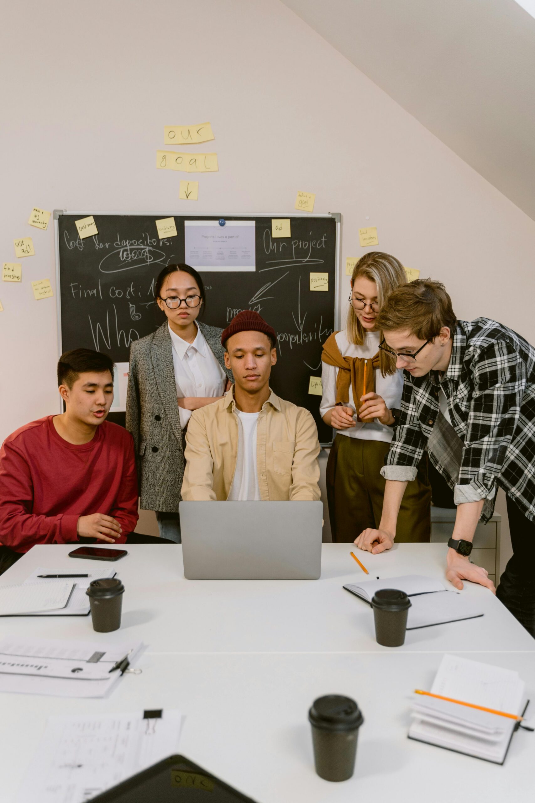 A diverse group of professionals engaged in a collaborative meeting around a laptop in an office setting.