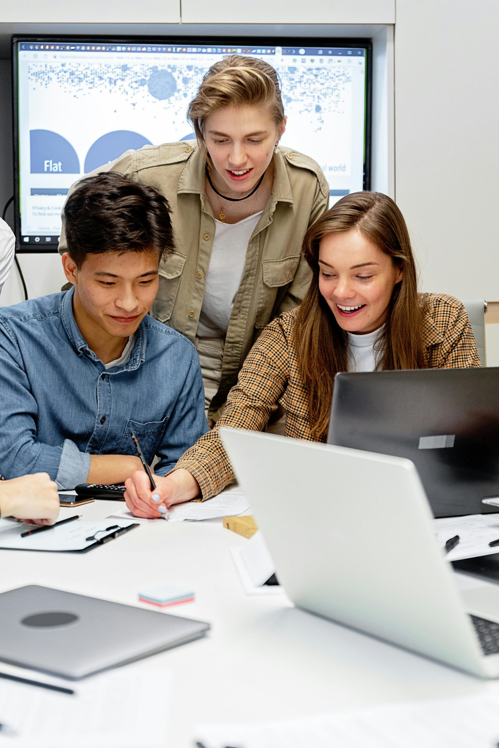 Three colleagues collaborating on a project with laptops in a modern office setting.